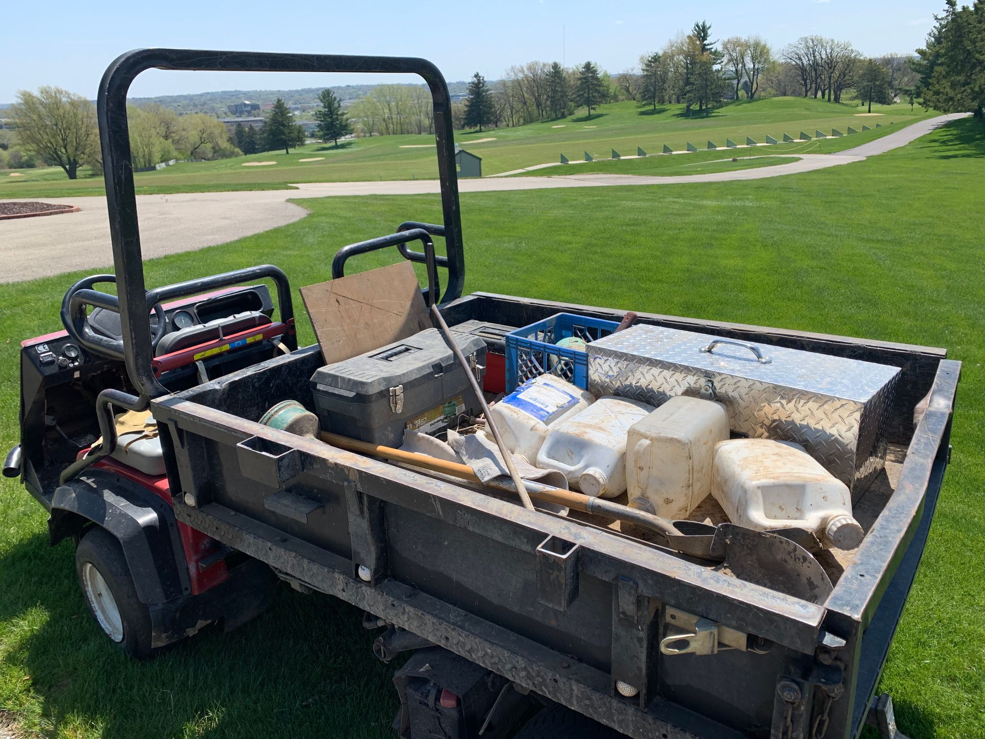 A utility vehicle with a trailer full of tools is parked on a golf course.