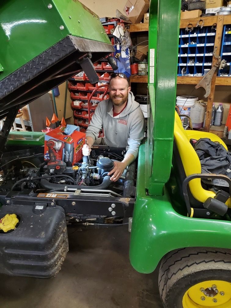 A man is working on a green tractor in a garage.