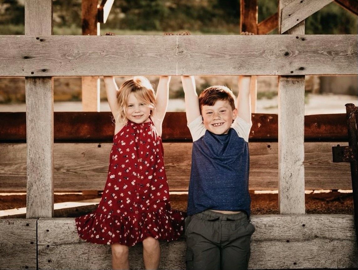 A boy and a girl are sitting next to each other on a wooden fence.