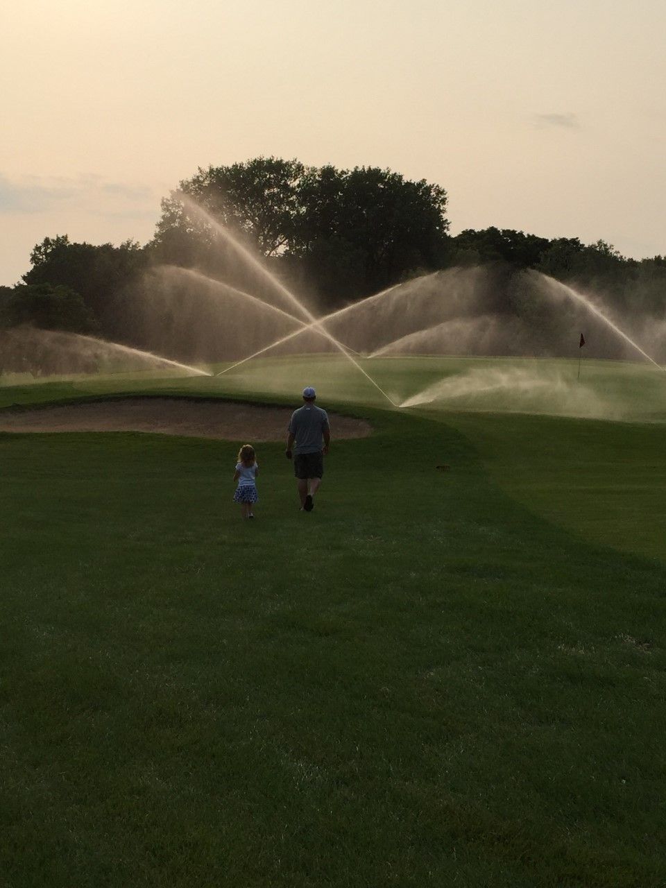 A man and a little girl are walking on a golf course