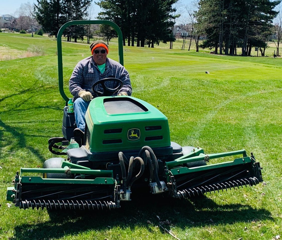 A man is riding a green john deere lawn mower on a lush green field.