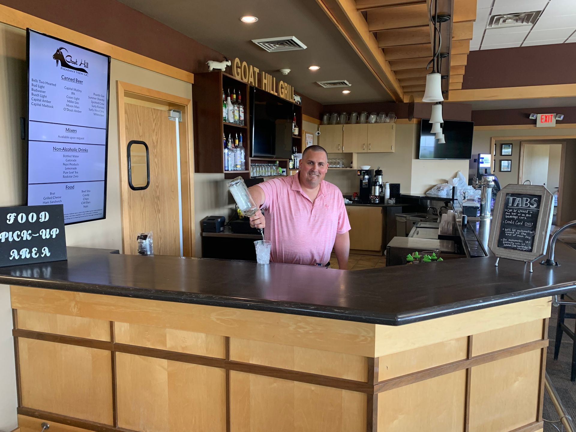 A man in a pink shirt is standing behind a bar in a restaurant.