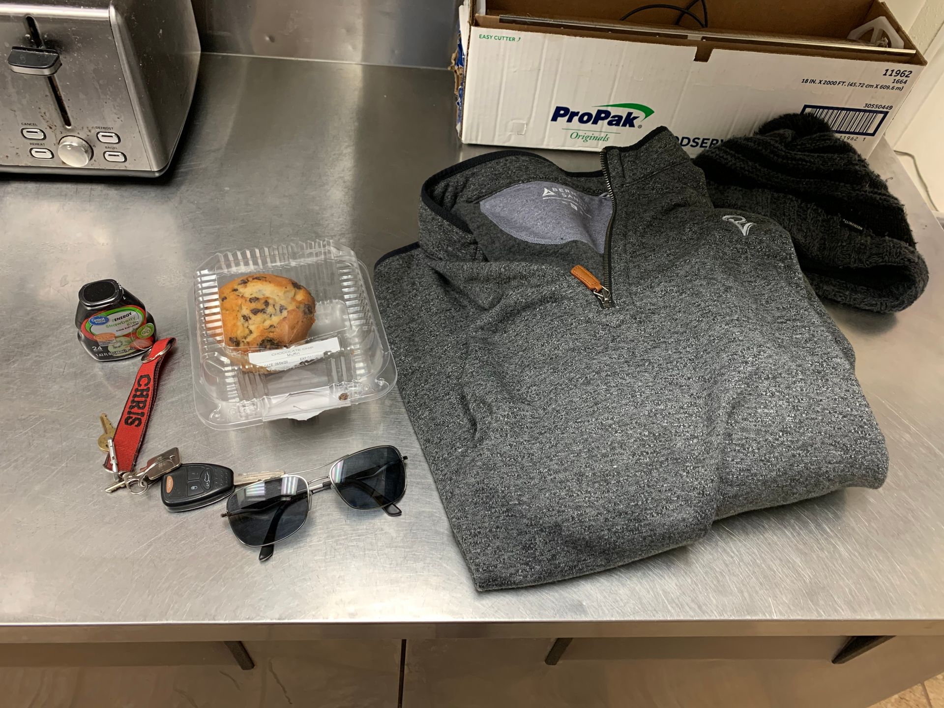 A table with a jacket , sunglasses , keys , a cookie and a toaster.