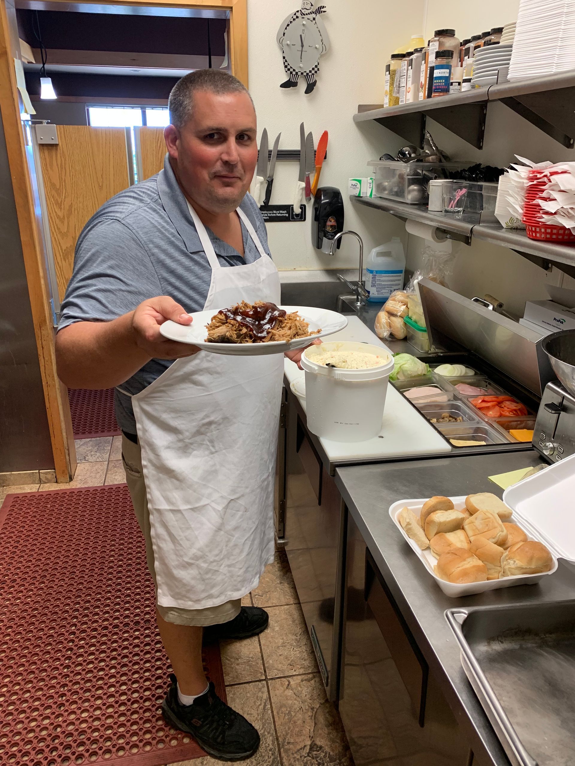 A man in an apron is holding a plate of food in a kitchen.