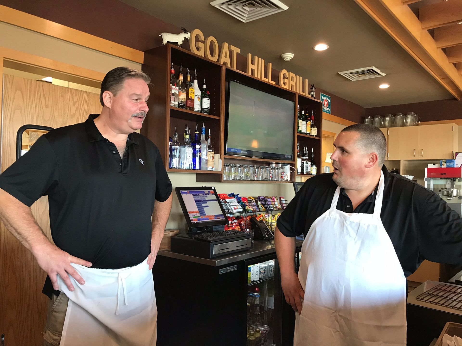 Two men are standing in a restaurant talking to each other.