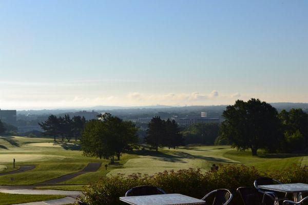 A view of a golf course with tables and chairs in the foreground