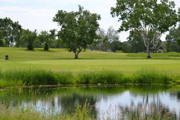 A golf course with trees and a pond in the foreground.