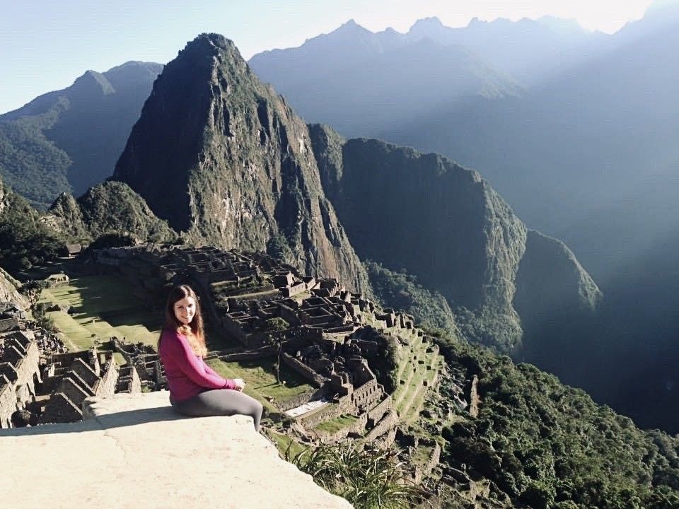 A woman sits on a ledge overlooking a mountain range