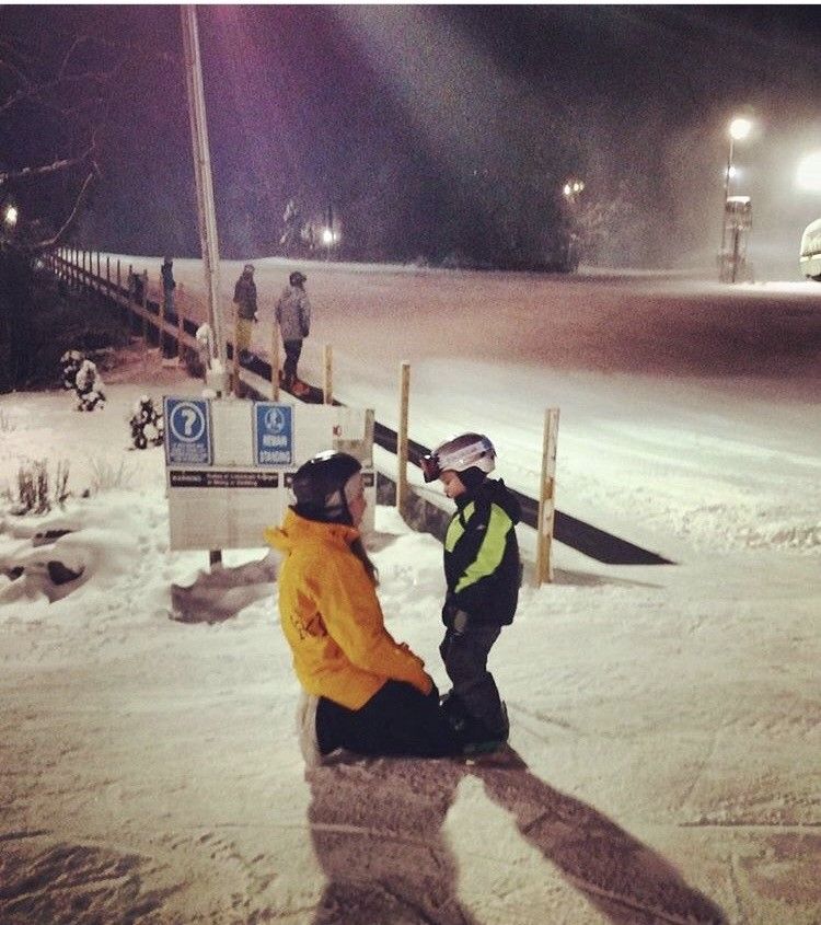 A man in a yellow jacket sits next to a child in a snowy area