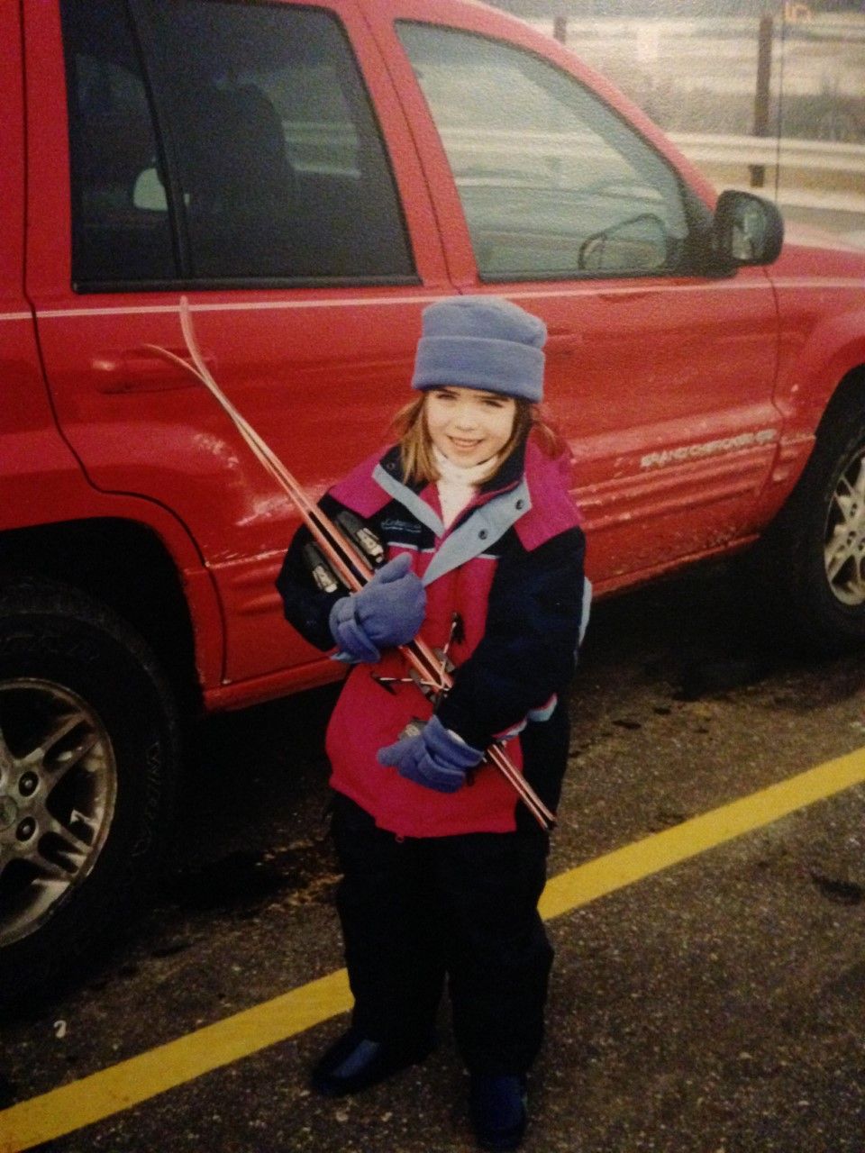 A little girl is holding skis in front of a red car