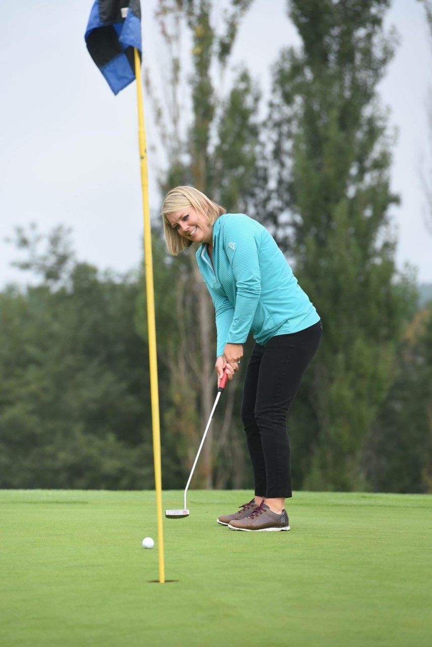 A woman is putting a golf ball on a green.