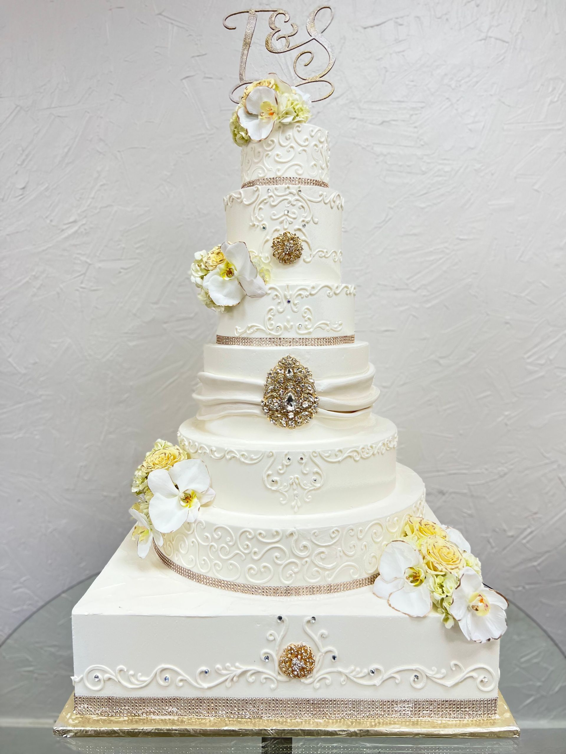 a large white wedding cake with flowers on it is sitting on top of a glass table .