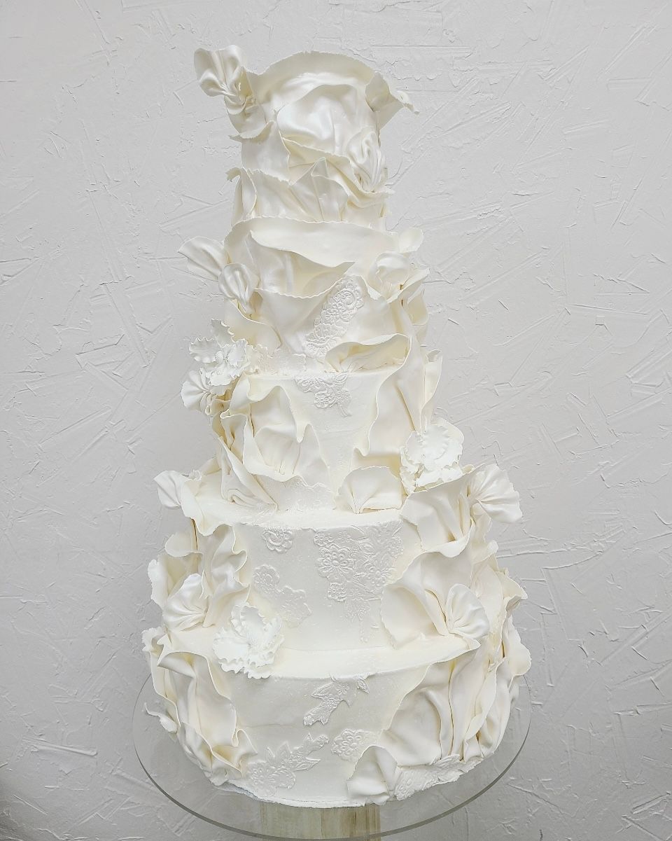 a white wedding cake is sitting on top of a glass cake stand .