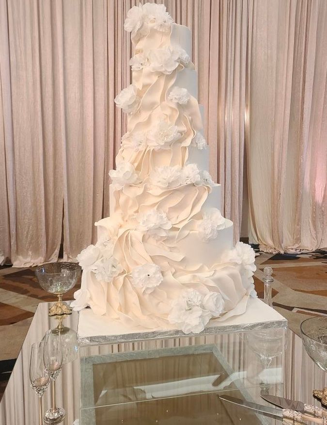 a white wedding cake is sitting on top of a glass table .