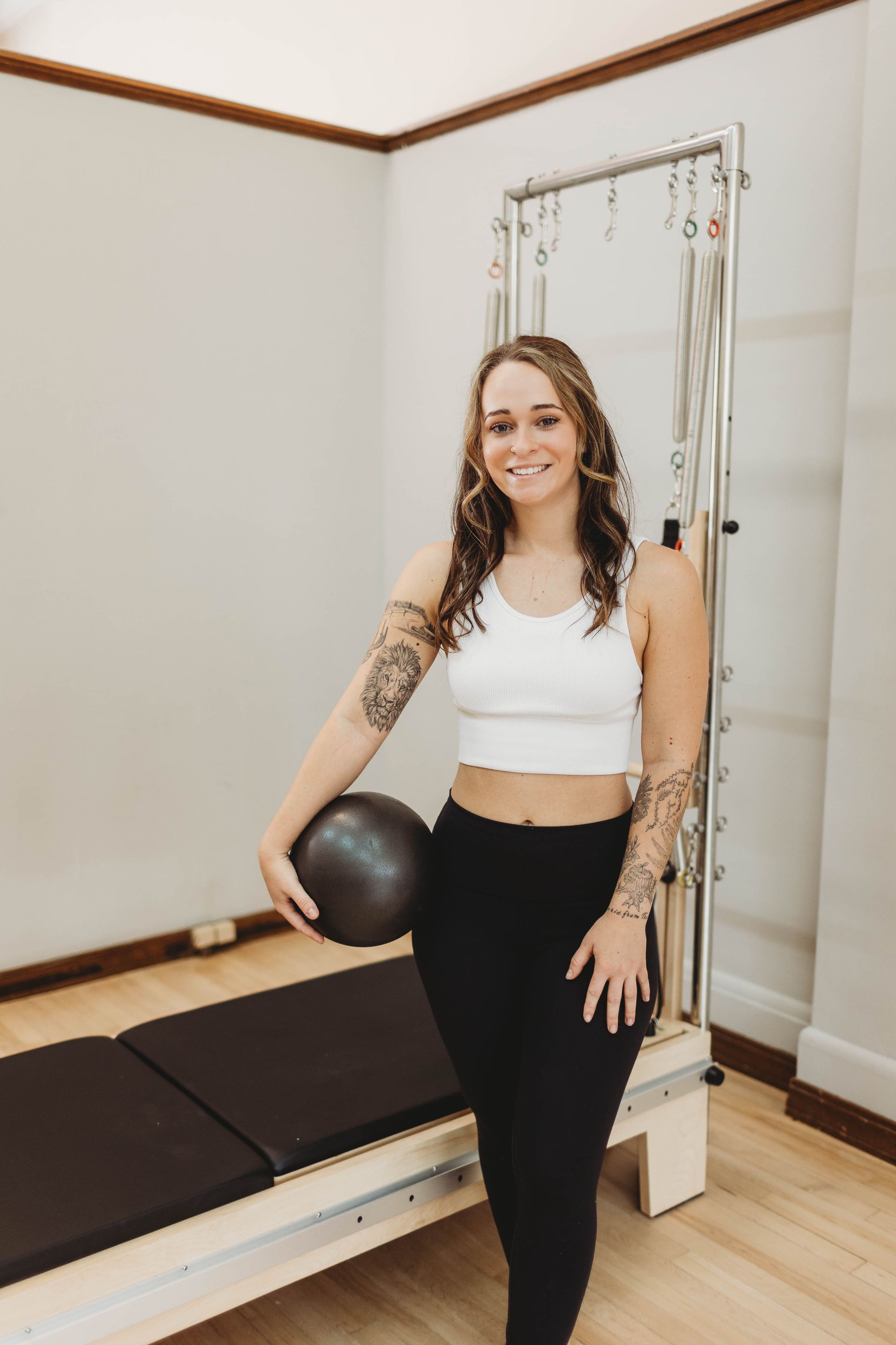 A woman is standing next to a pilates machine holding a ball.