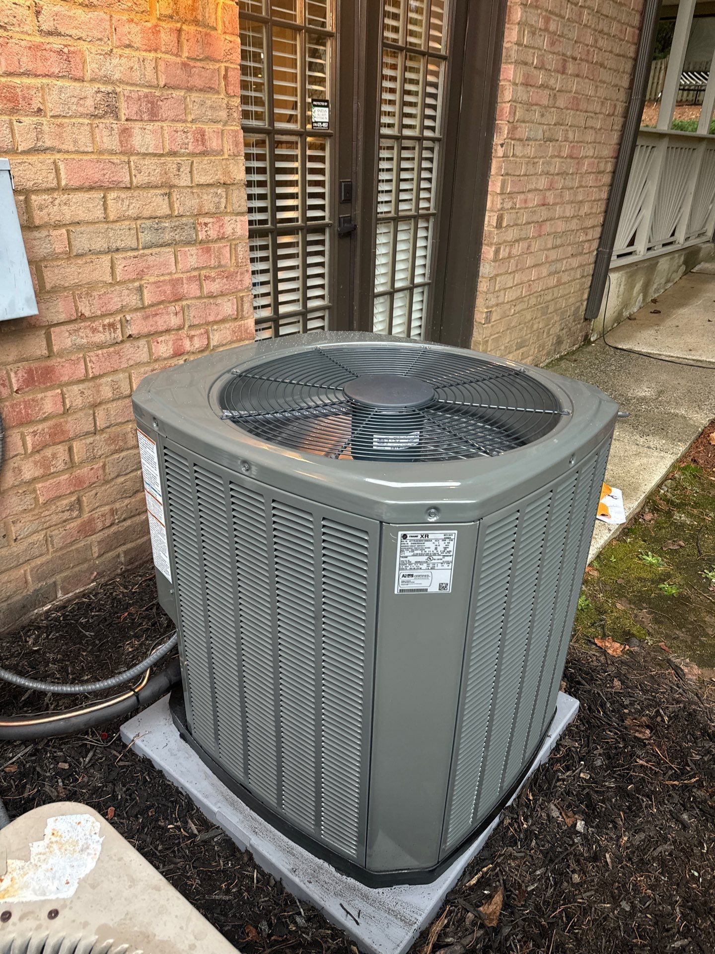 A large air conditioner is sitting outside of a brick building.