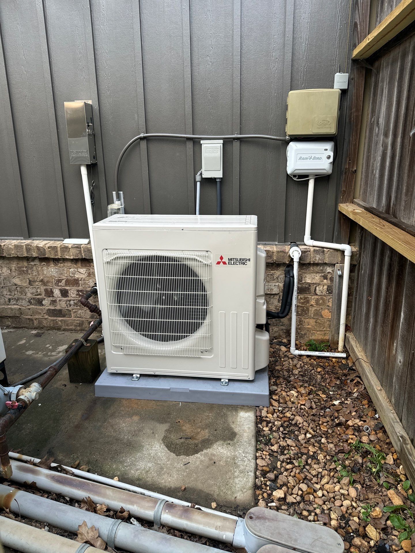 A white air conditioner is sitting on the ground next to a fence.