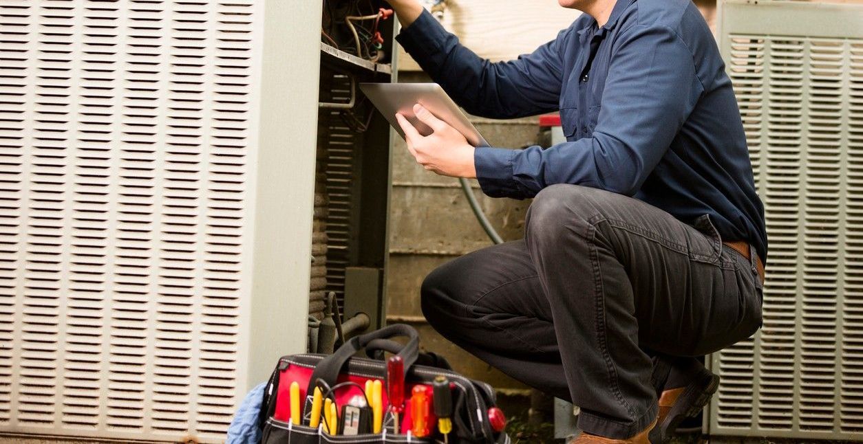 A man is kneeling down and working on an air conditioner.