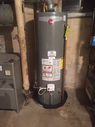 A water heater is sitting in a basement next to a furnace.