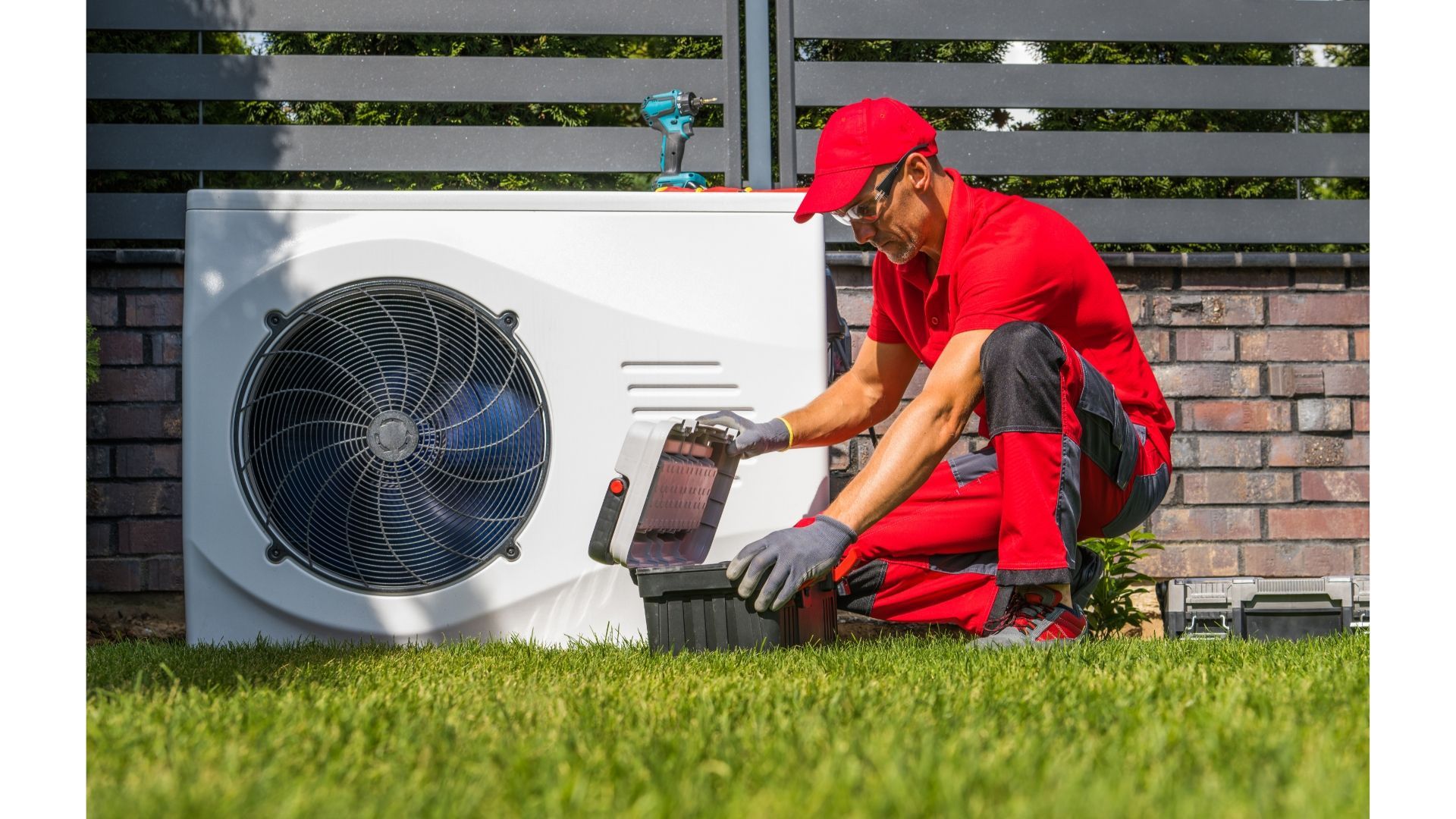 A man is kneeling in the grass next to a fan.