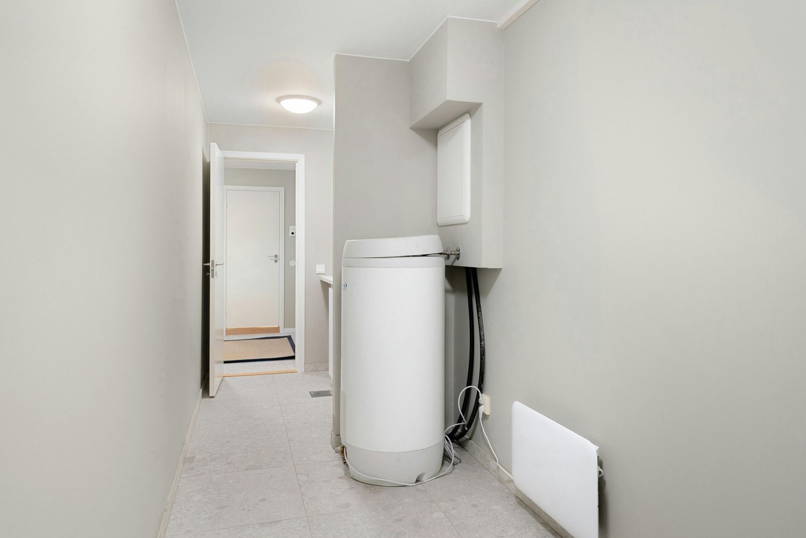 A white water heater is sitting in a hallway next to a door.
