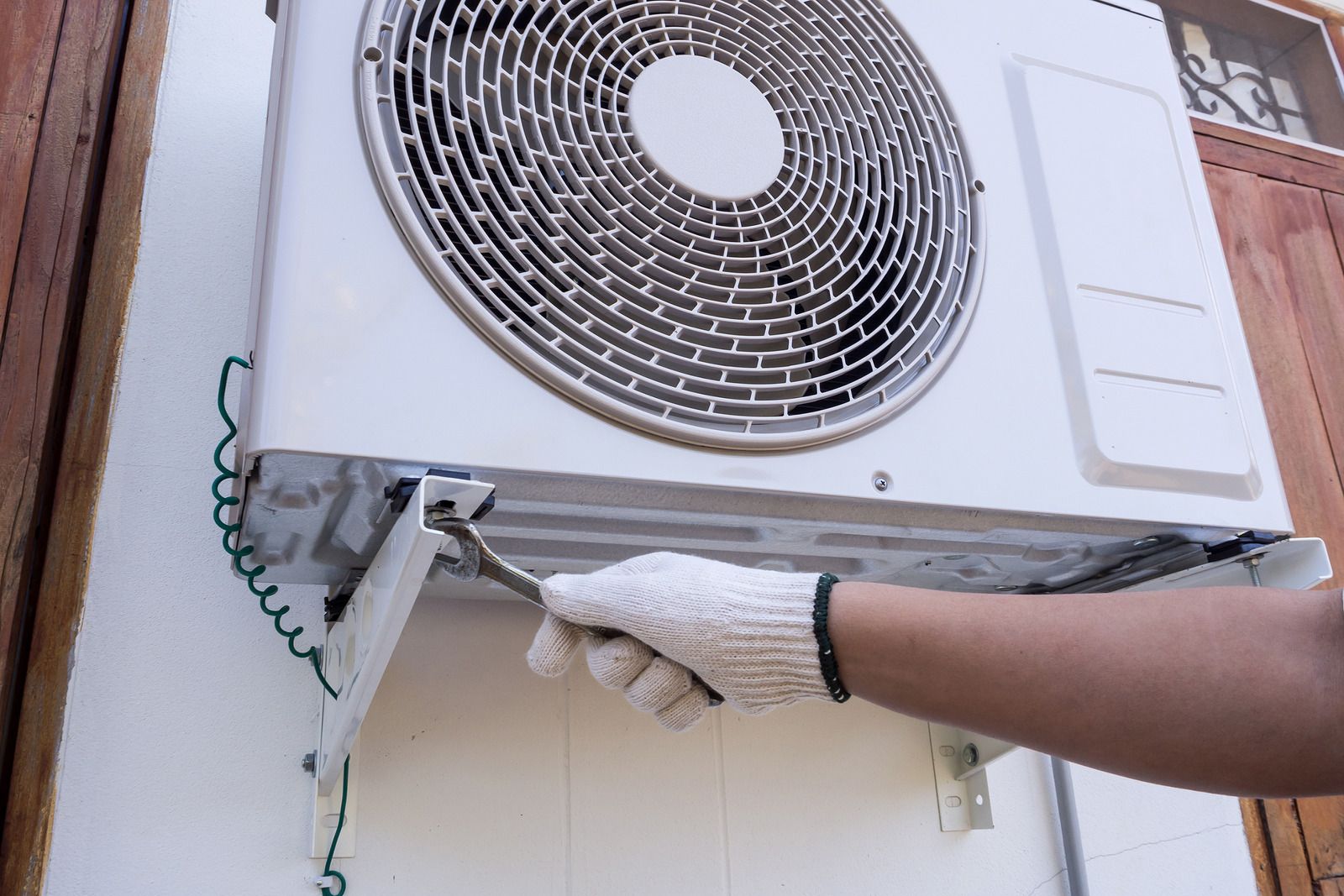 A person is working on an air conditioner on the side of a building.