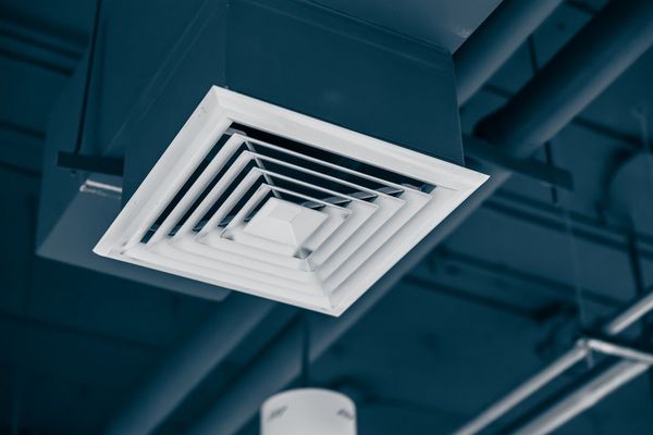 A white air vent is hanging from the ceiling of a building.