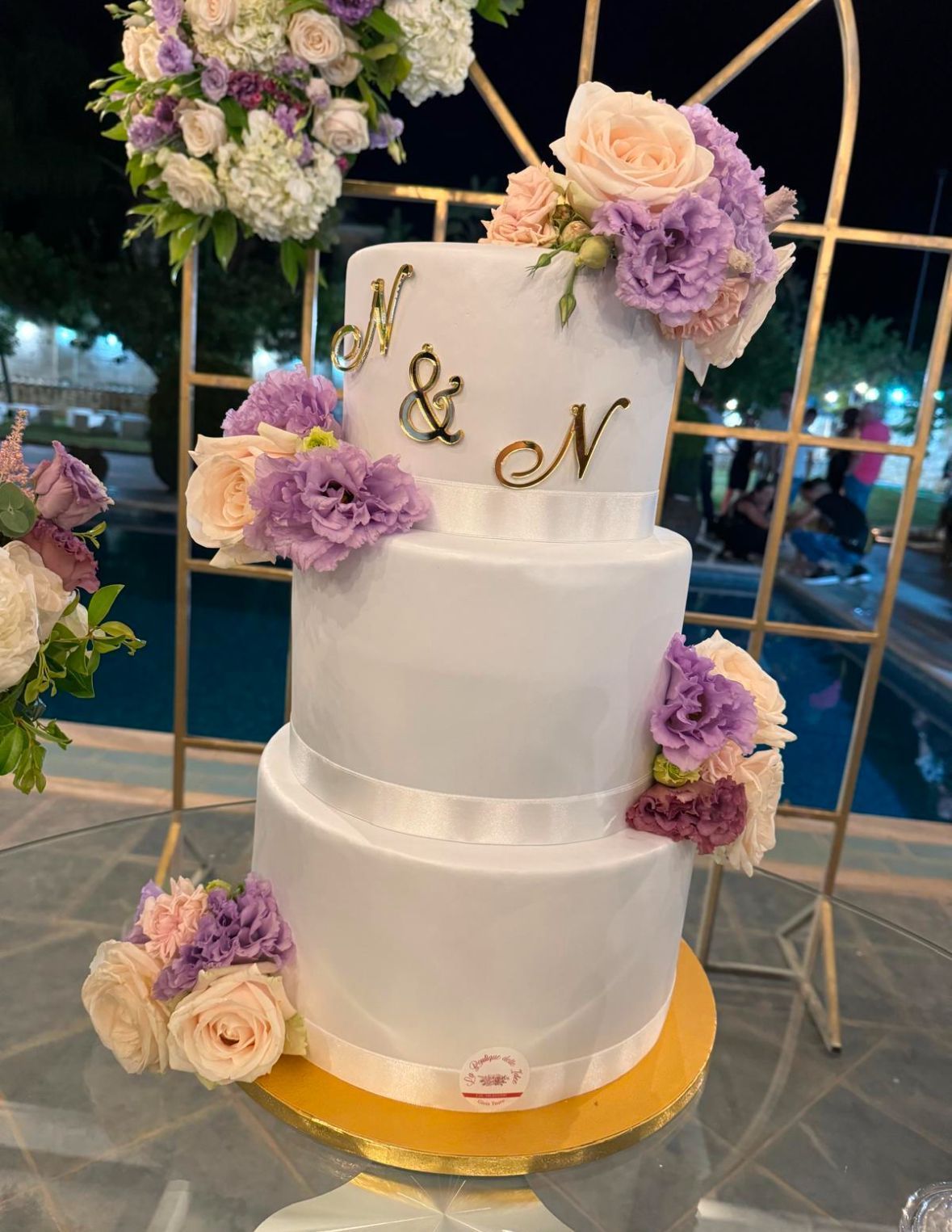 Una torta nuziale bianca con fiori viola e lettere sopra
