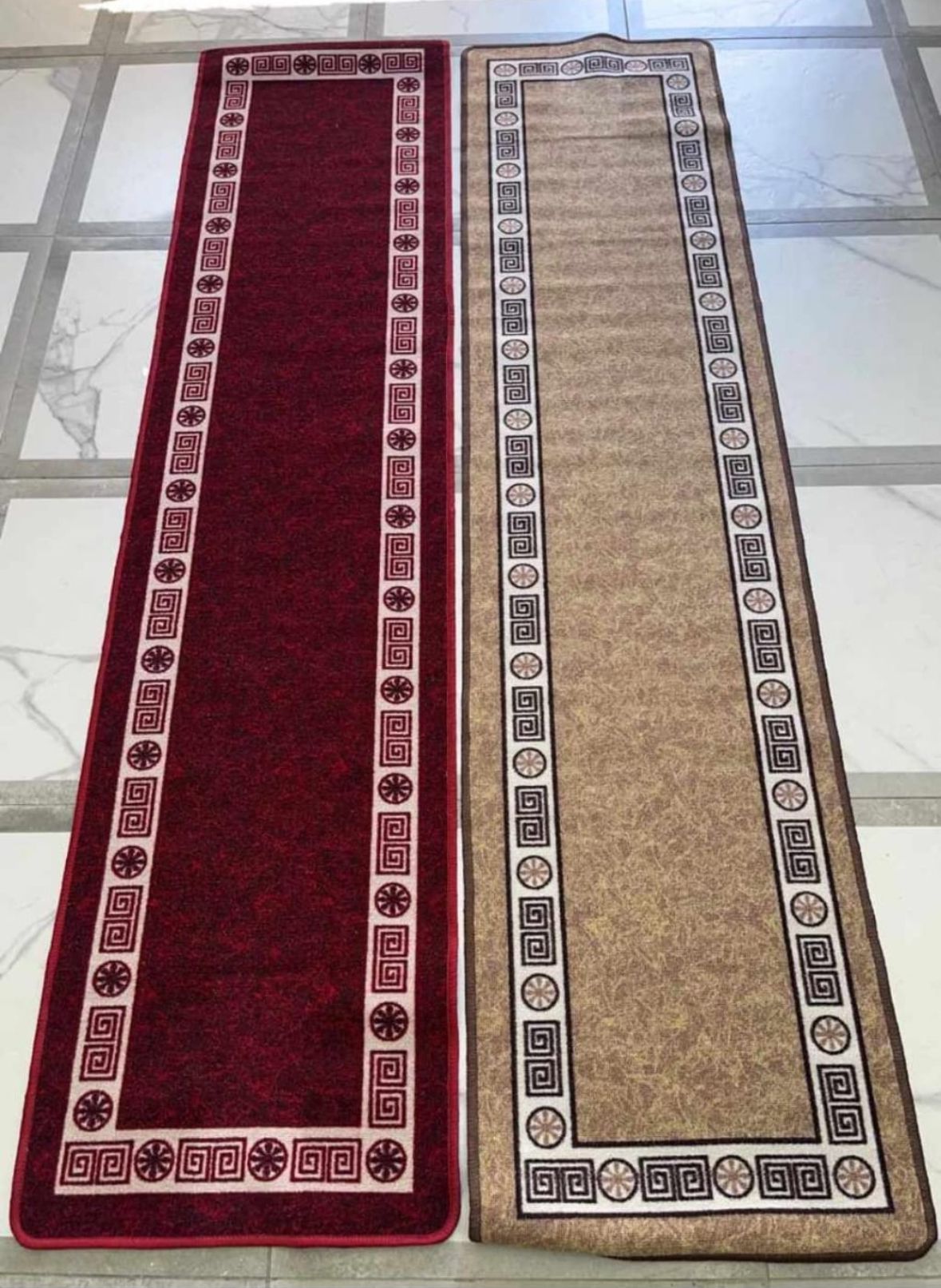 Un tappeto rosso e uno marrone sono appoggiati uno accanto all'altro su un pavimento piastrellato.