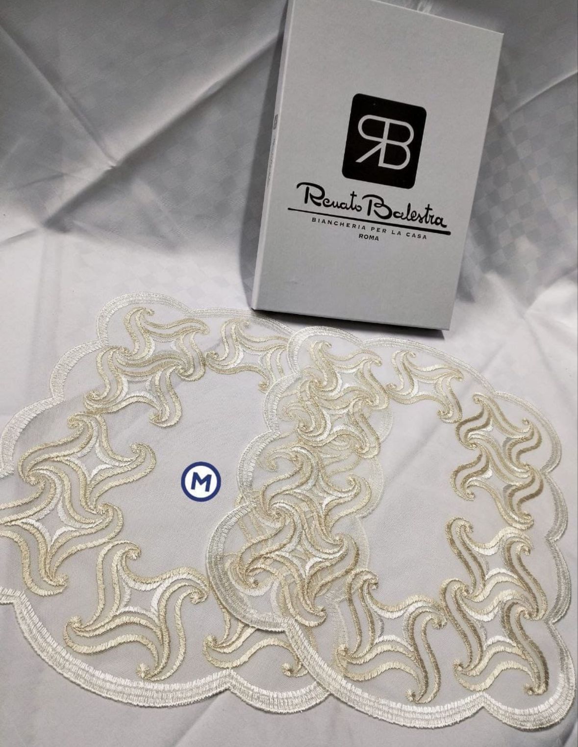 Una tovaglia bianca ricamata è appoggiata su un tavolo accanto a una scatola.