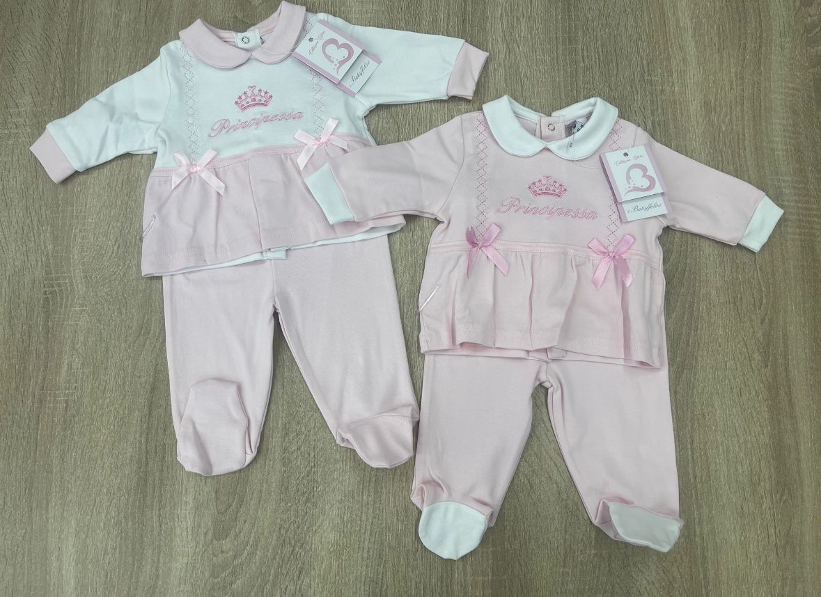 Due vestitini rosa e bianchi per neonati sono appoggiati su un tavolo di legno.