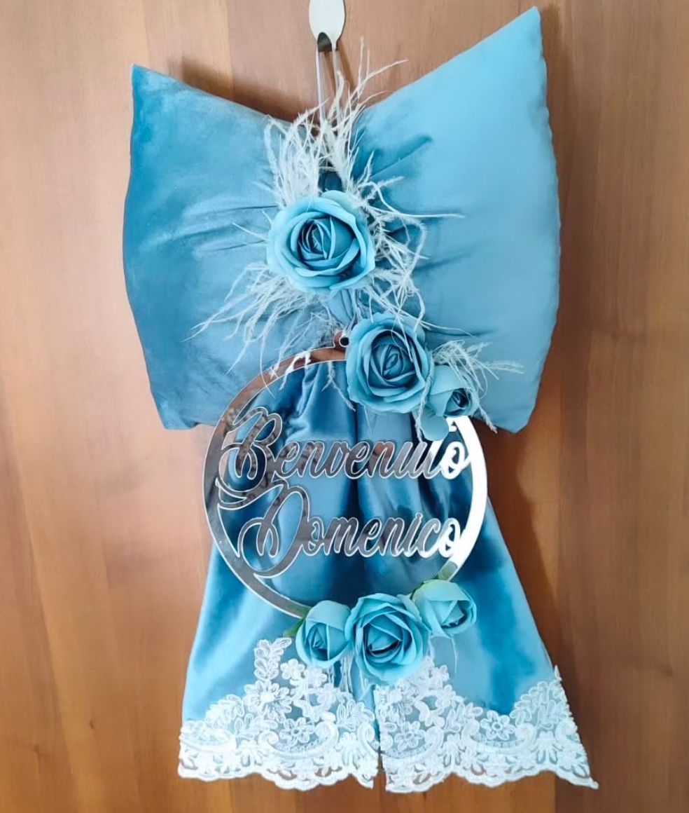 Un fiocco blu con fiori e pizzo è appeso a una parete di legno.