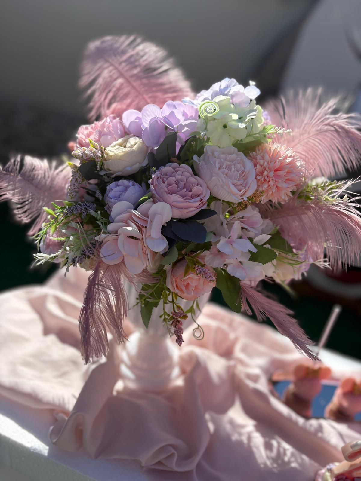 Un vaso pieno di fiori rosa e piume su un tavolo.