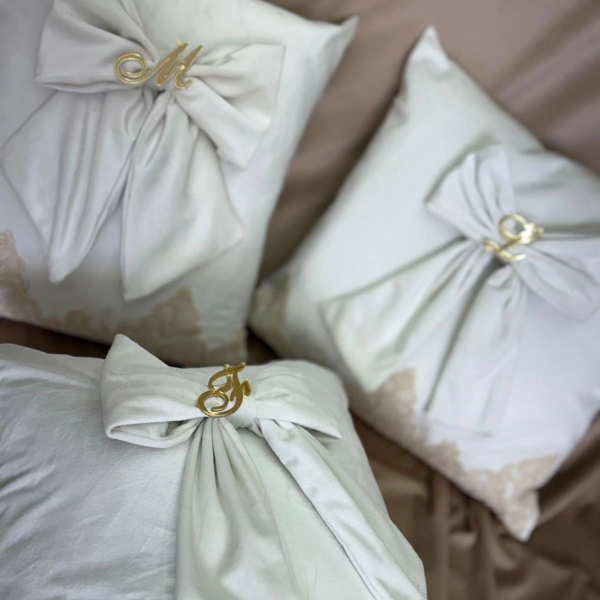 Tre cuscini bianchi con fiocchi e lettere sopra