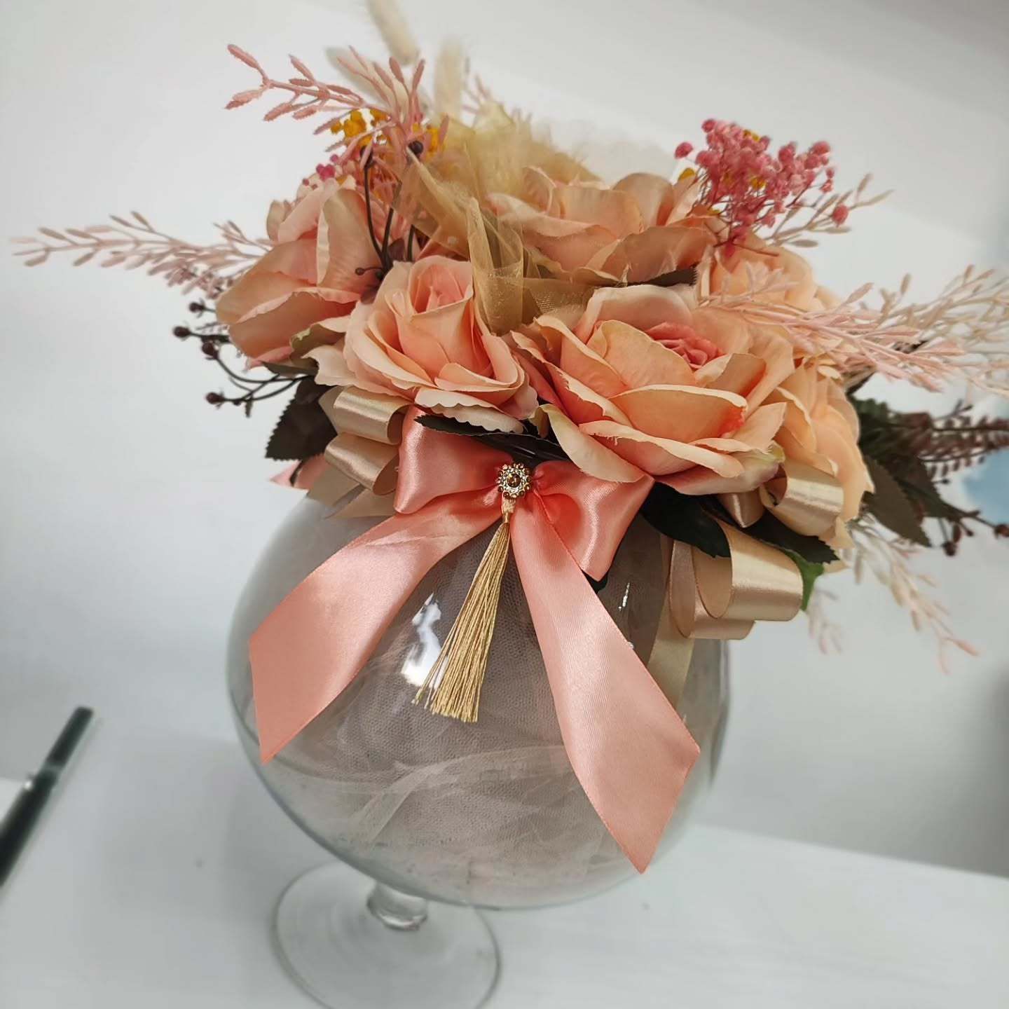 Un vaso pieno di fiori e un fiocco rosa