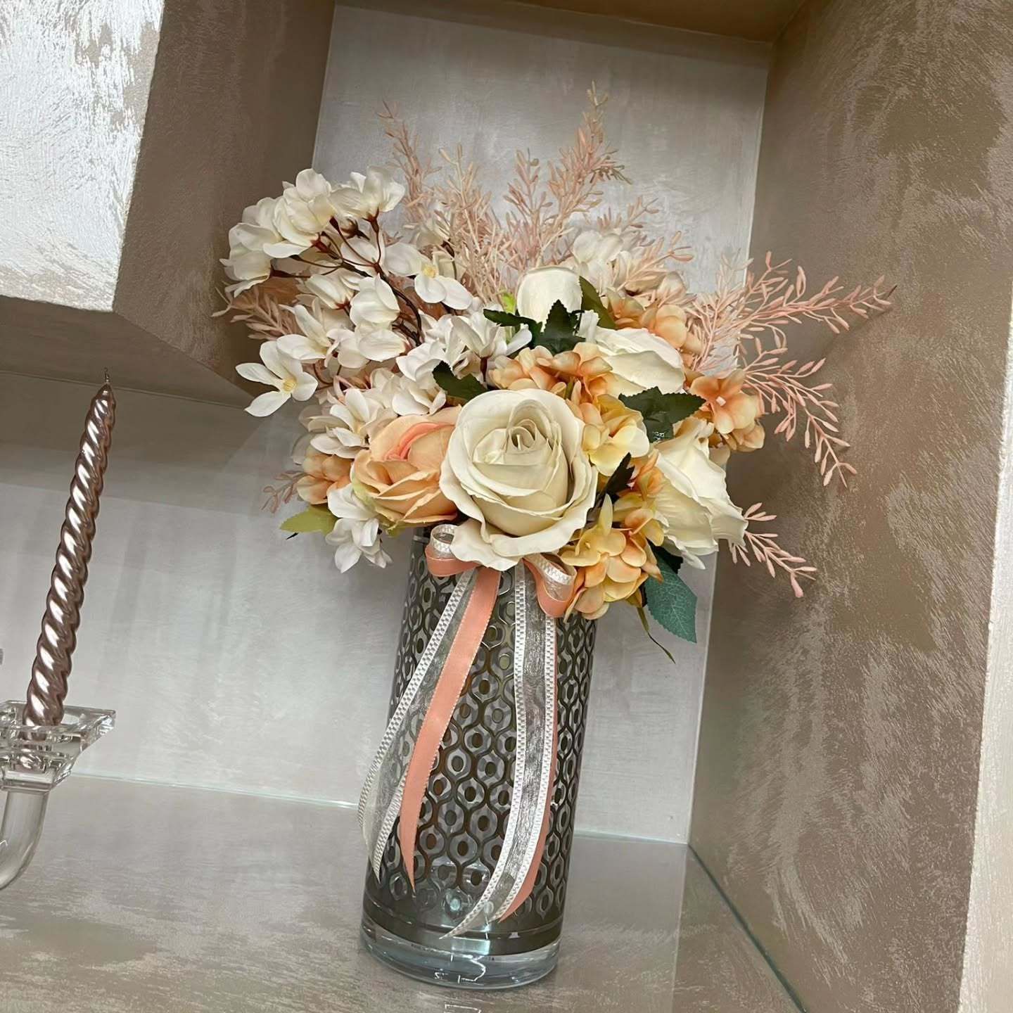 Un vaso pieno di fiori è appoggiato su un tavolo accanto a un portacandele.