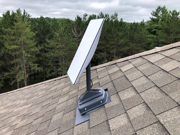 A satellite dish on top of a roof with trees in the background