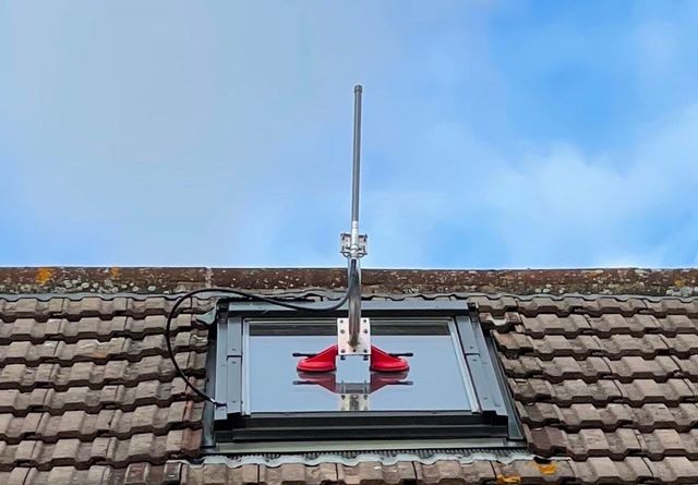 An antenna is sitting on top of a roof next to a window.