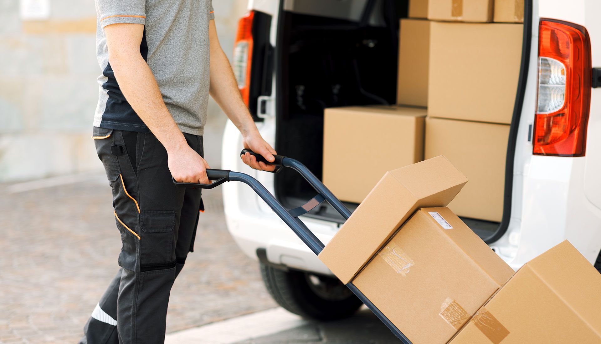 Delivery person loading boxes into a van using a hand truck.