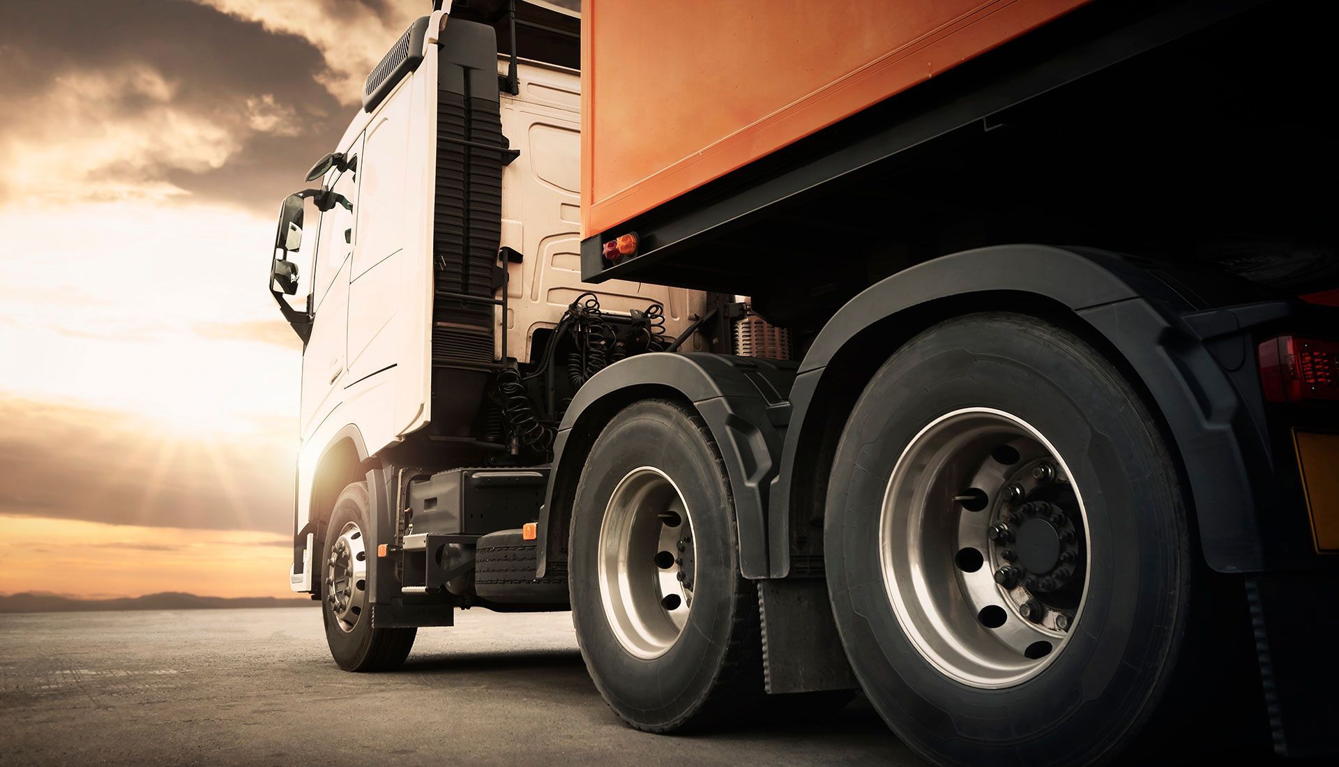 Semi-truck on a road at sunset, highlighting the wheels and cab.