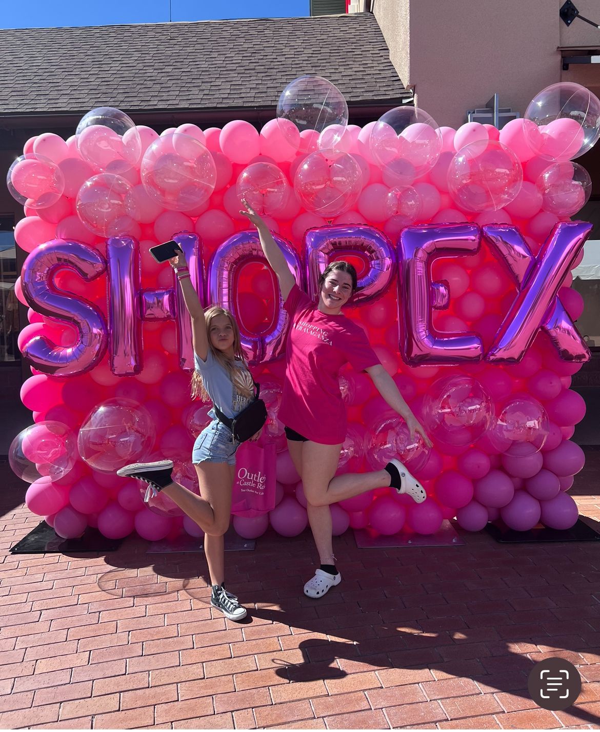 Two women standing in front of a wall of pink balloons that says shopex