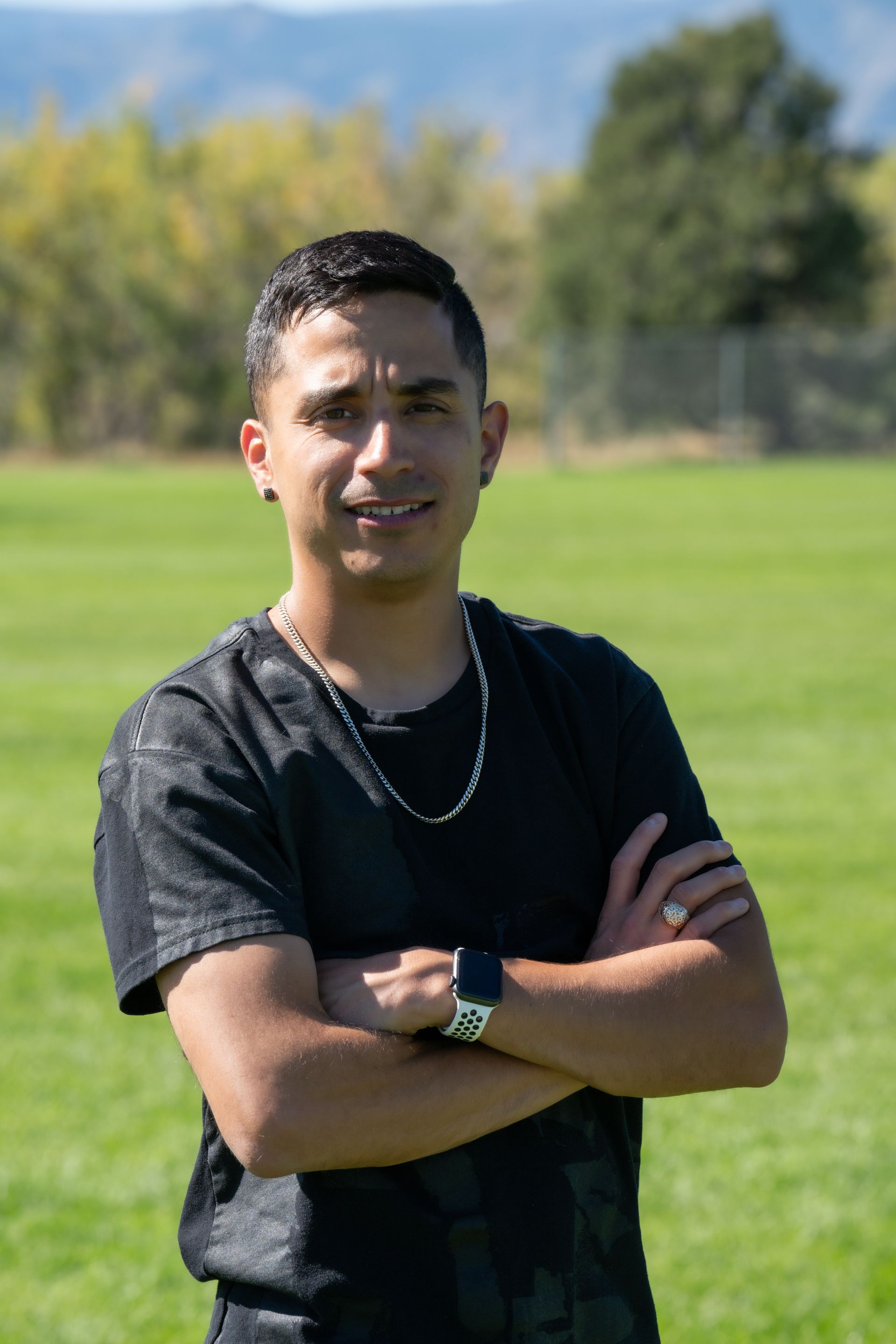 A young man is standing in a field with his arms crossed.