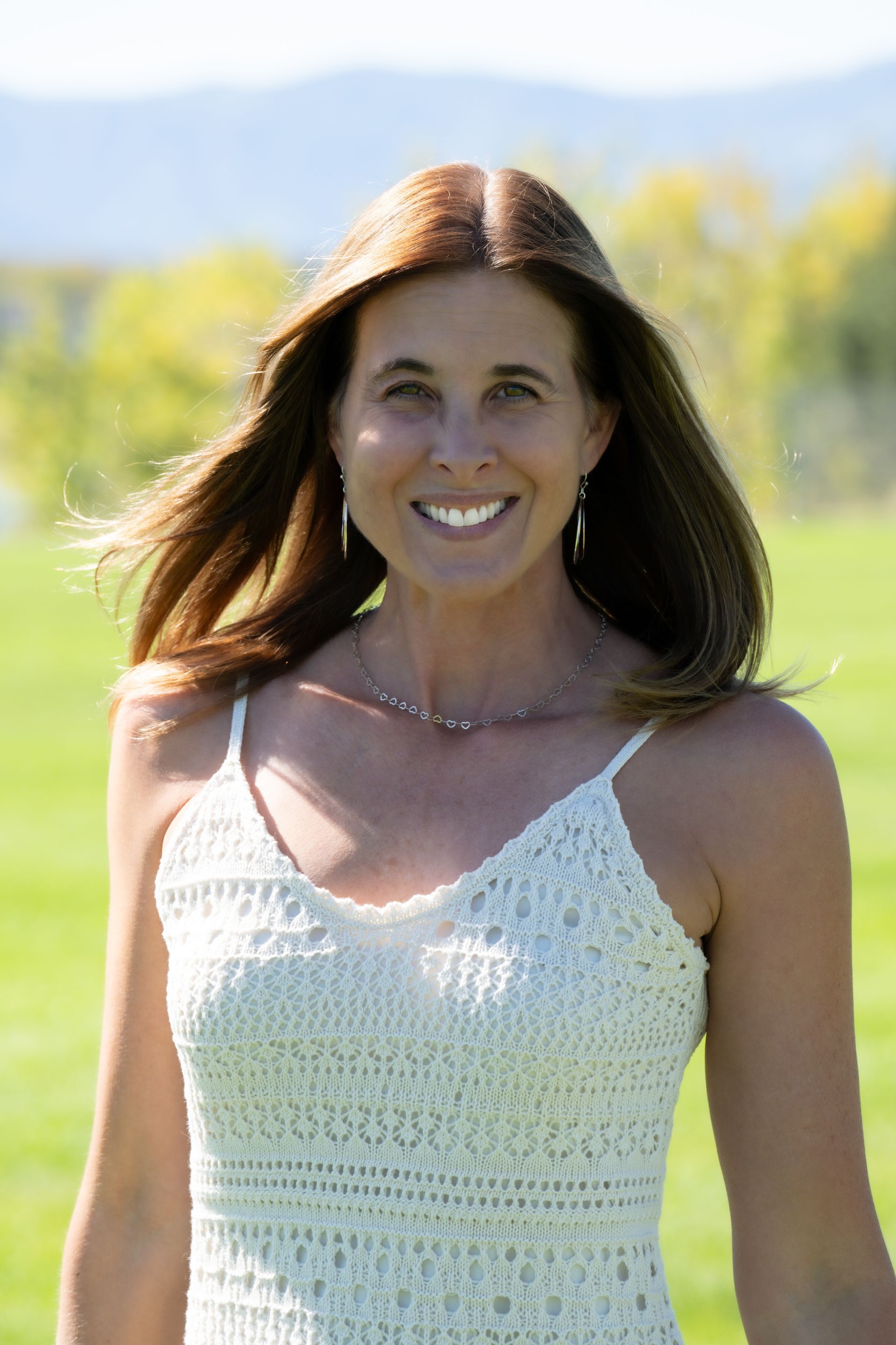 A woman in a white dress is smiling in a field.
