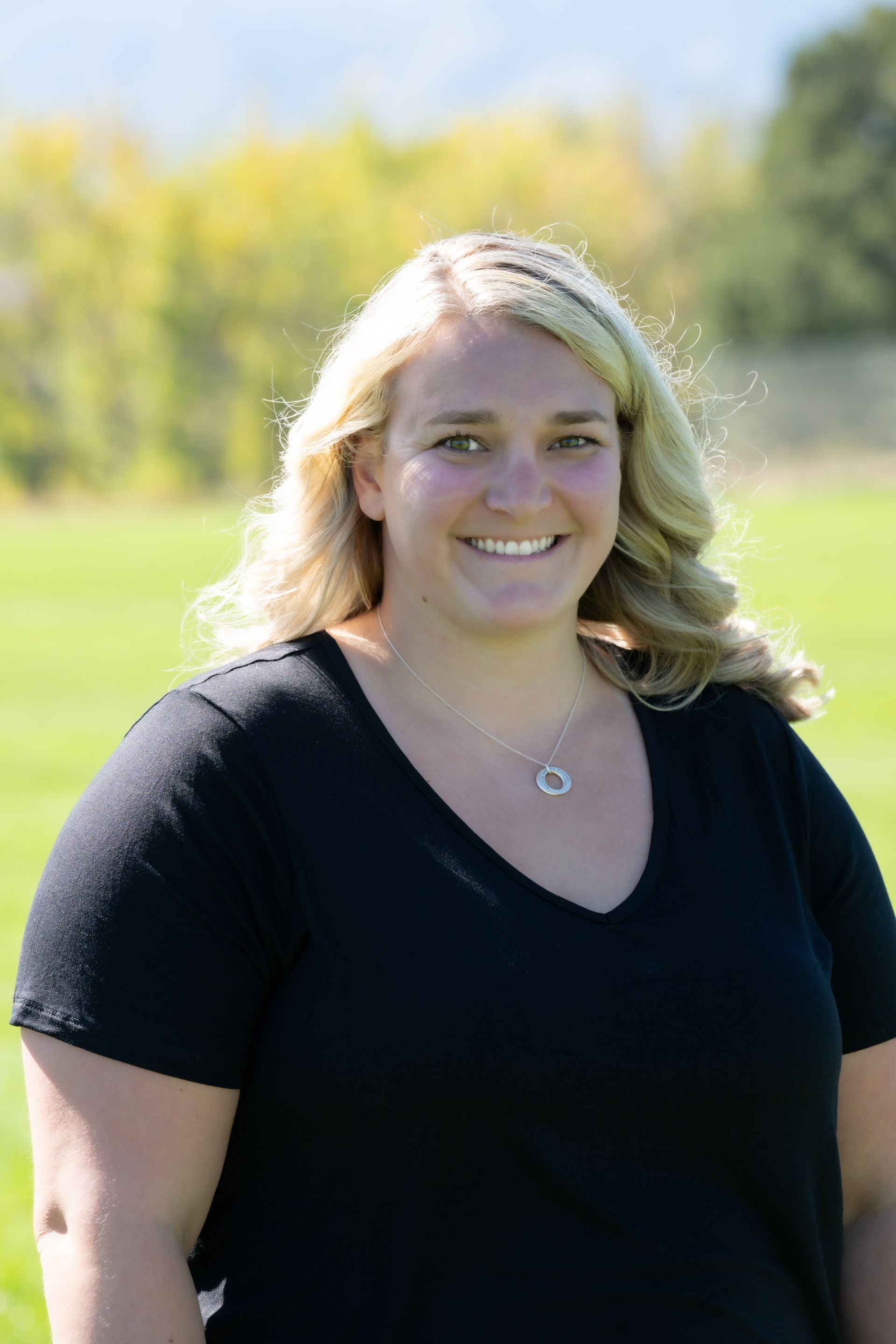 A woman in a black shirt is standing in a field and smiling.