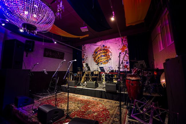 Een podium voor een muziekoptreden, met microfoons, instrumenten en een decoratieve achtergrond in een slecht verlichte zaal.