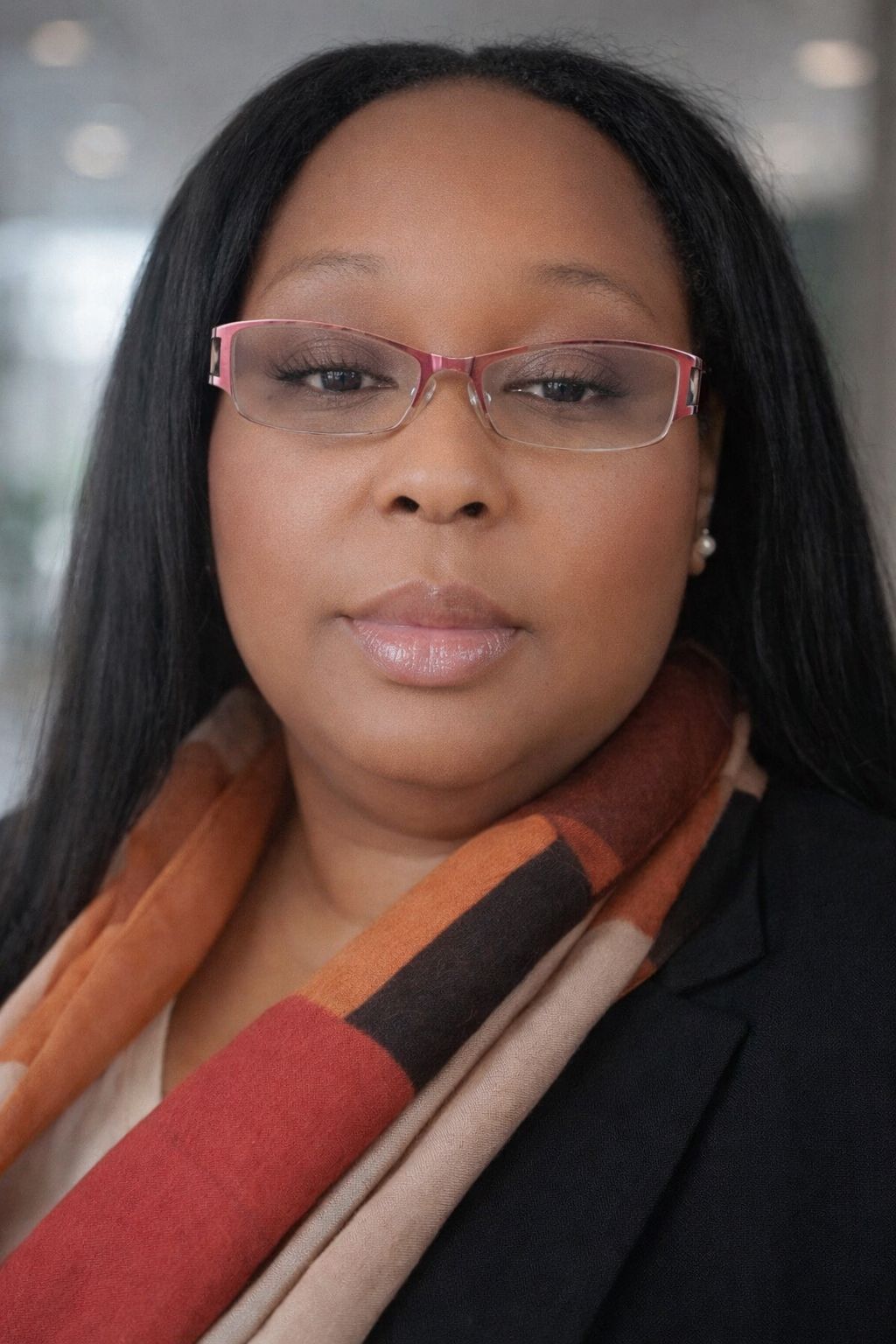A professional headshot of a person wearing glasses and a multi-colored scarf, looking directly at the camera.