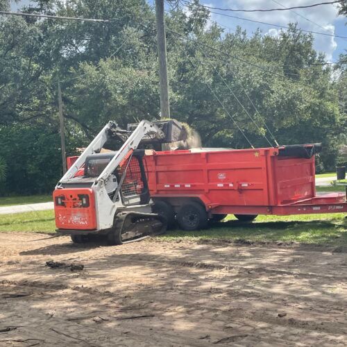 Orange Bobcat skid steer loading a red dump trailer with debris outdoors.