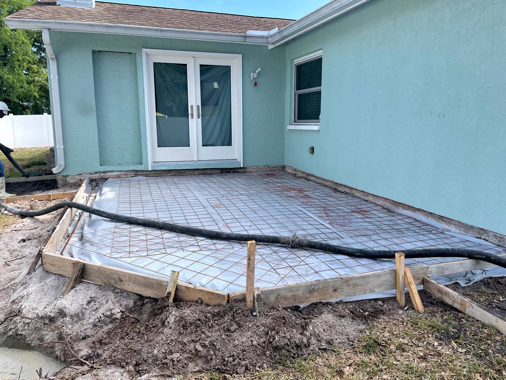 Construction site: concrete patio form next to a blue house with glass doors.