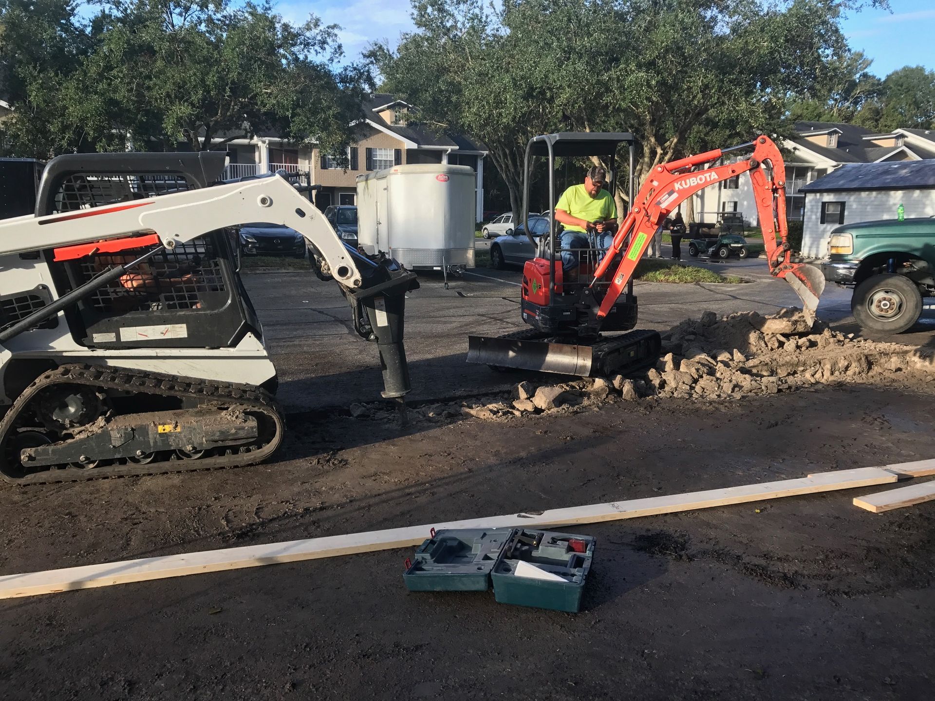 Construction site: Bobcat, excavator, and worker digging in asphalt.