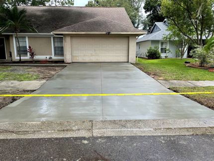 Freshly poured gray concrete driveway in front of a beige house with a closed garage door, yellow caution tape.